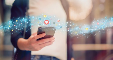 A hand holding a phone with a graphic stream of social media icons across the image.